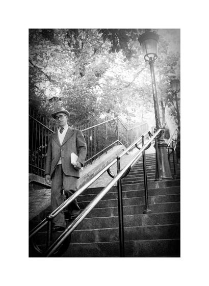 Ein Mann in Anzug und Hut läuft eine Treppe herunter und hält ein Buch in der Hand. Über ihm Bäume, in der Mitte ein Treppen Geländer. Das Foto ist sw und im Stil der 50 er Jahre