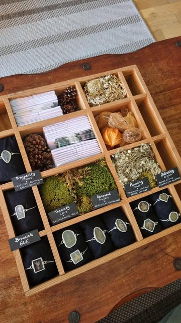 English A kind of wooden drawer with several compartments filled with moss, lichen, dried fruits, and stained glass bracelets containing pressed leaves.
Français Un genre de tiroir en bois avec plusieurs casiers remplis de mousse, de lichen, de fruits séchés mais aussi de bracelets en vitrail contenant des feuilles pressées.