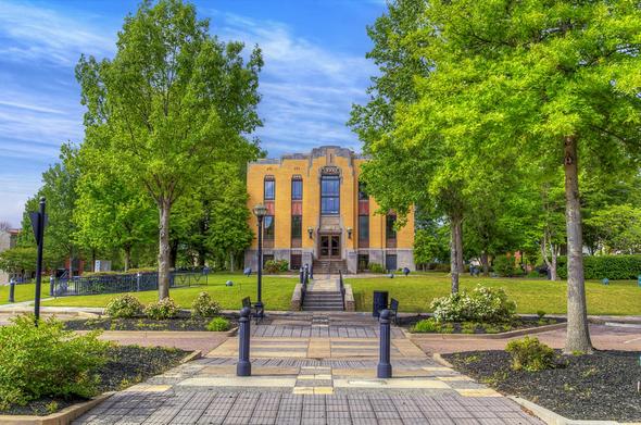 Lauderdale County Courthouse Among the Trees

A brick courthouse with large windows sits at the end of a symmetrical pathway, surrounded by lush green trees and colorful flowerbeds.