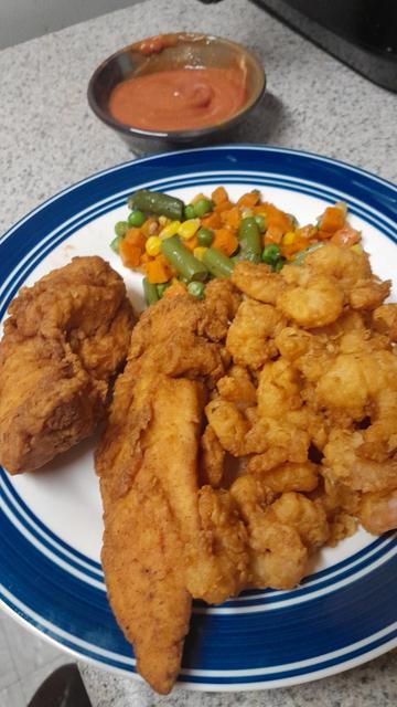 Plate with breaded fried chicken tenders, popcirn shrimp and mixed vegetables and behind it a small bowl with ketchup and dijon mustard mix.