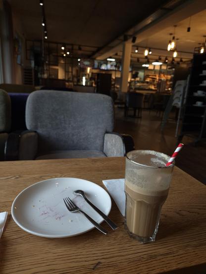 The image depicts a scene in a cozy indoor setting, featuring a table adorned with a plate and a glass of coffee.  Various objects are also present in the image, such as a chair, a beverage, tableware, kitchen utensils, and a dining table. The setting suggests a moment of relaxation or enjoyment, perhaps in a coffee shop or restaurant. The image evokes a sense of comfort and familiarity, inviting the viewer to imagine themselves in a similar setting, savoring a delicious beverage.