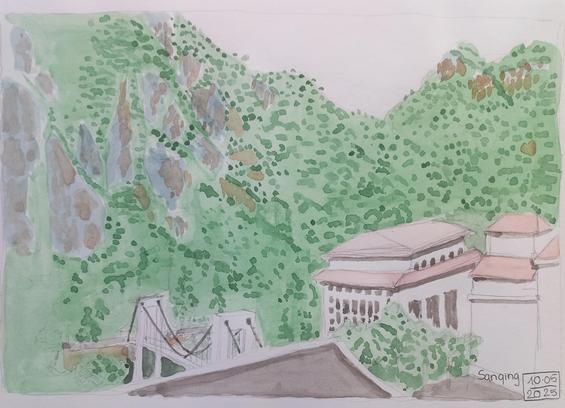 Une rangé de montagnes avec des rochers et de la verdure. En contrebas un complexe hôtelier et un pont suspendu.
A mountain range with rocks and greenery and below some hotel buildings with a suspended bridge.