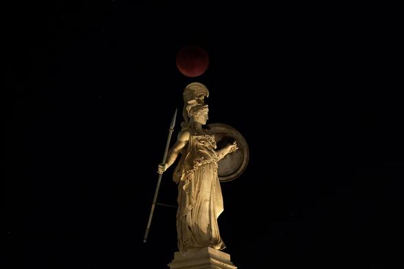 A full moon rises during an eclipse behind the statue of ancient Athena goddess in Athens, Greece, September 7. REUTERS/Louiza Vradi

The statue of Athena is white marble and depicts the goddess in a sleeveless flowing robe. She's wearing an elaborate plumed helmet, and is standing with her spear in her slightly outstretched behind her right arm, and her Aegis held with her left hand, also slightly outstretched. The reddish ("Blood") full moon in eclipse is just above her.