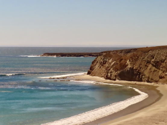 Pacific Ocean meets the coast of California under clear blue skies. 