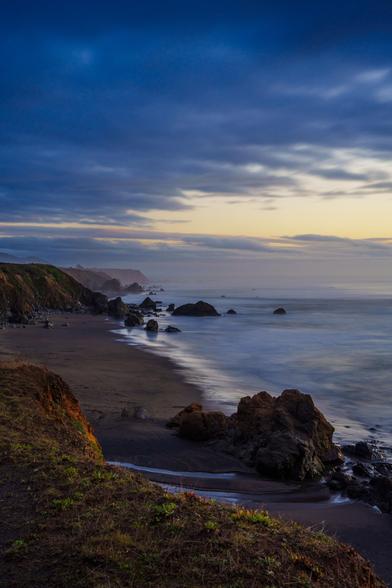 A serene beach at dusk, with gentle waves lapping at rocky shores under a cloudy sky.