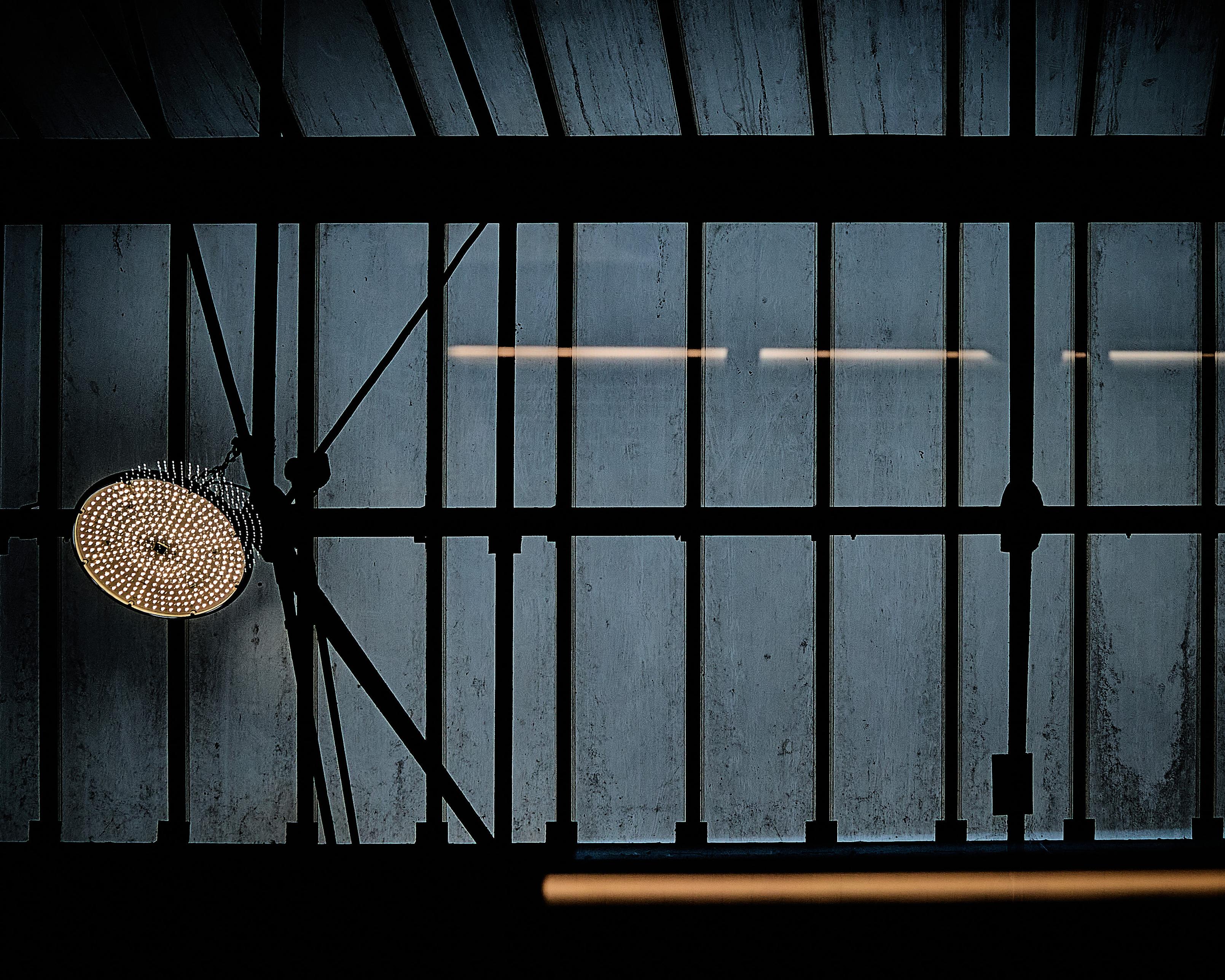 The image shows the interior view of a roof at Crewe Station, seen from inside a train. The roof's iron beams form a grid pattern, and the glass panes appear grimy, casting a dull light. A circular light fixture is visible, adding contrast against the grid The image shows the interior view of a roof at Crewe Station, seen from inside a train. The roof's iron beams form a grid pattern, and the glass panes appear grimy, casting a dull light. A circular light fixture is visible, adding contrast against the grid