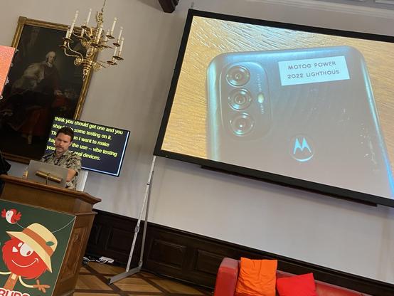 Scott on stage, with a slide showing an old Motorola device behind him