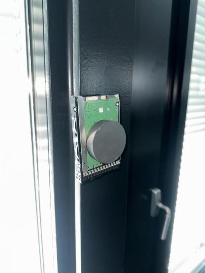 Eine 2.5" Festplatte in einem Hot-Swap-Rahmen klebt mit einem Magneten von rund 5cm Durchmesser und einem Zentimeter Dicke an einem Metallpfosten.