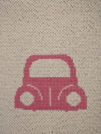 Partial frame of a pink truck cross stitched on white fabric with little gold filaments woven in.