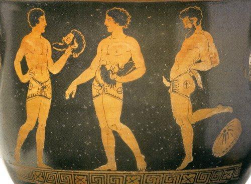 Red-figure vase painting of three male actors, all of whom wear trunks with an erect phallus. Two of them hold the mask of a satyr, seemingly talking to each other, while a third has already put on his mask and flaunts the phallus on his trunks.