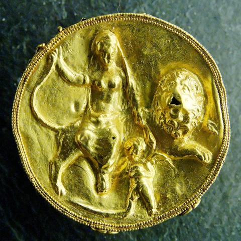 Golden medallion with Aphrodite sitting on a male, maned lion. Winged Eros stands in the front.