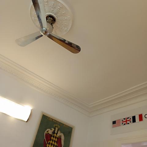 Schnappschuss 
Ein stylischer, dreiflügliger verchromter Deckenventilator (etwa 2 Meter Durchmesser!)
Decken - Axel mit Stuck, Wandleuchte gegenüber 
ein Teil eines Werbeplakats "Cremant du Roi" Grafik Oberkörper eines Königs 
Rechte Seite d. Fotos Hinweisschild mit den ehemaligen 3 Westberliner Alliierten Schutzmächte 🇺🇸🇬🇧🇫🇷
 
(Nicht sichtbarer Teil d. Hinweisschild:
 "
Allied
Checkpoint
Charlie
"
)