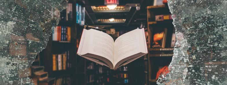 A book floating in mid-air behind a shattered pane of shatterproof glass.