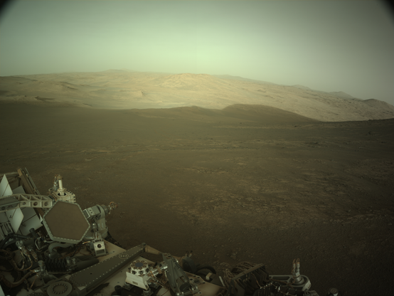 An ochre toned image capturing a shadowy Martian landscape, with the Perseverance rover in the foreground.