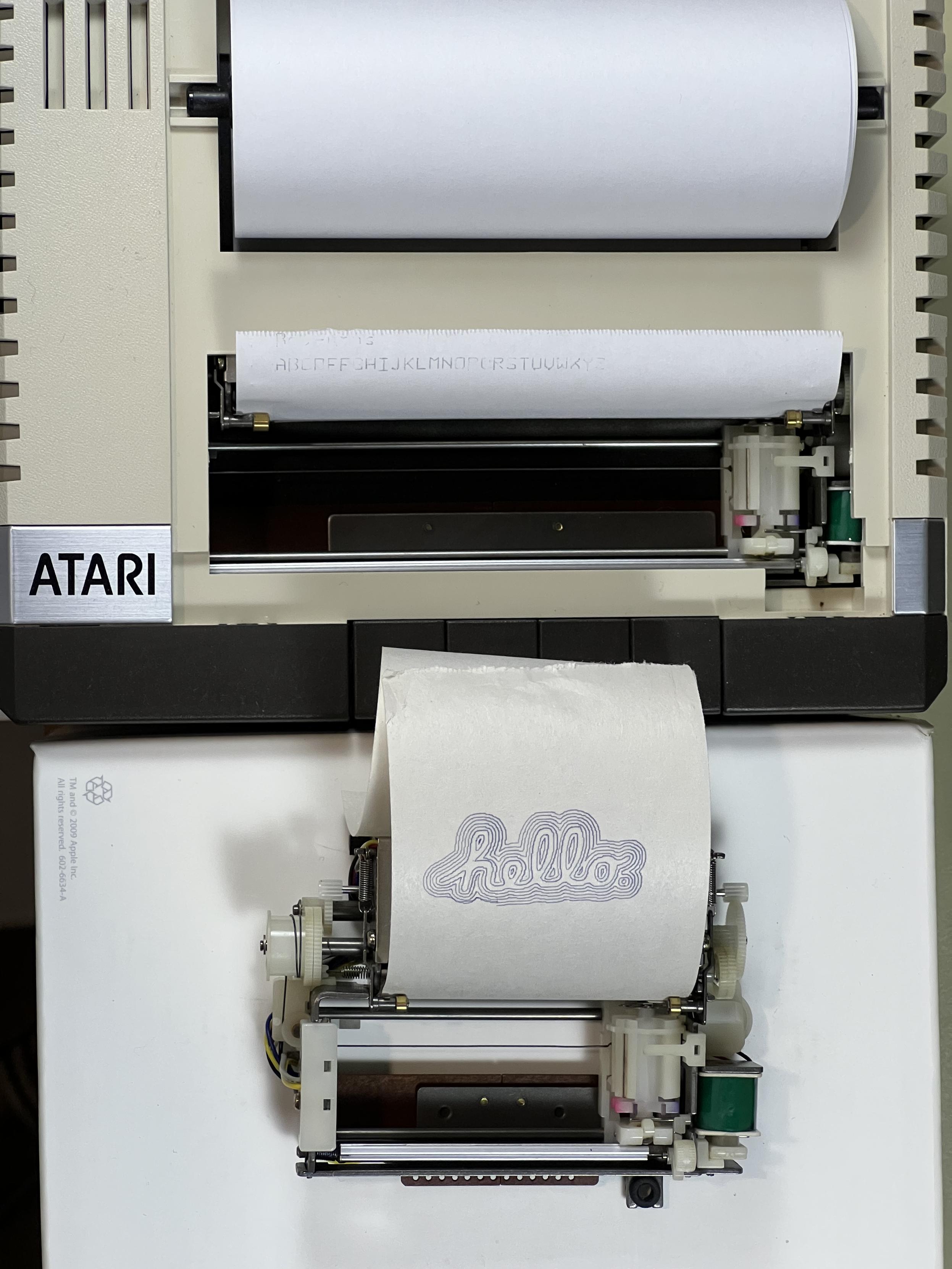 An Atari 1020 plotter on top, open with paper loaded and a bare ALPS mechanism below, smaller, with smaller paper loaded.