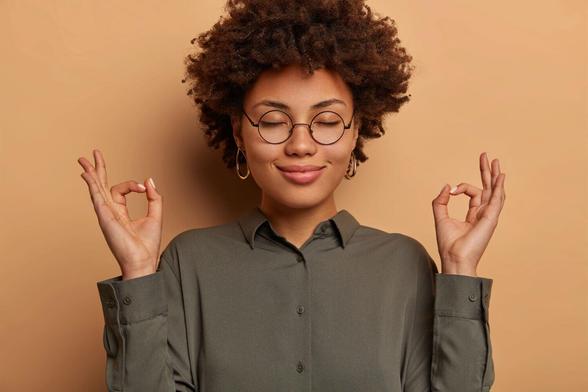Smiling woman with eyes closed practicing meditation with hands in mudra gesture against a warm background