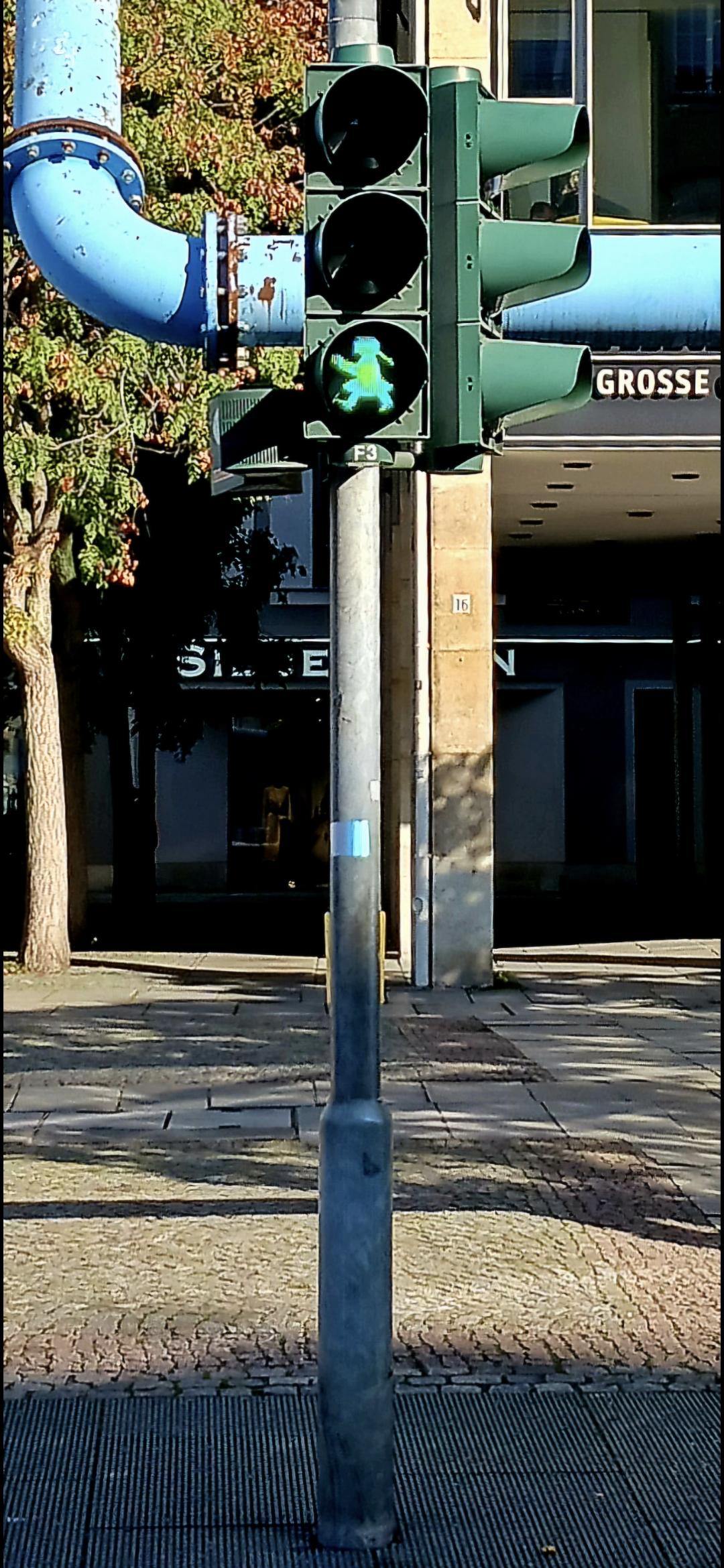 Straßenbild an einer Ampel. Im Mittelpunkt steht ein grün leuchtendes Ampelmädchen im Hintergrund eine Einkaufsstraße. Straßenbild an einer Ampel. Im Mittelpunkt steht ein grün leuchtendes Ampelmädchen im Hintergrund eine Einkaufsstraße.