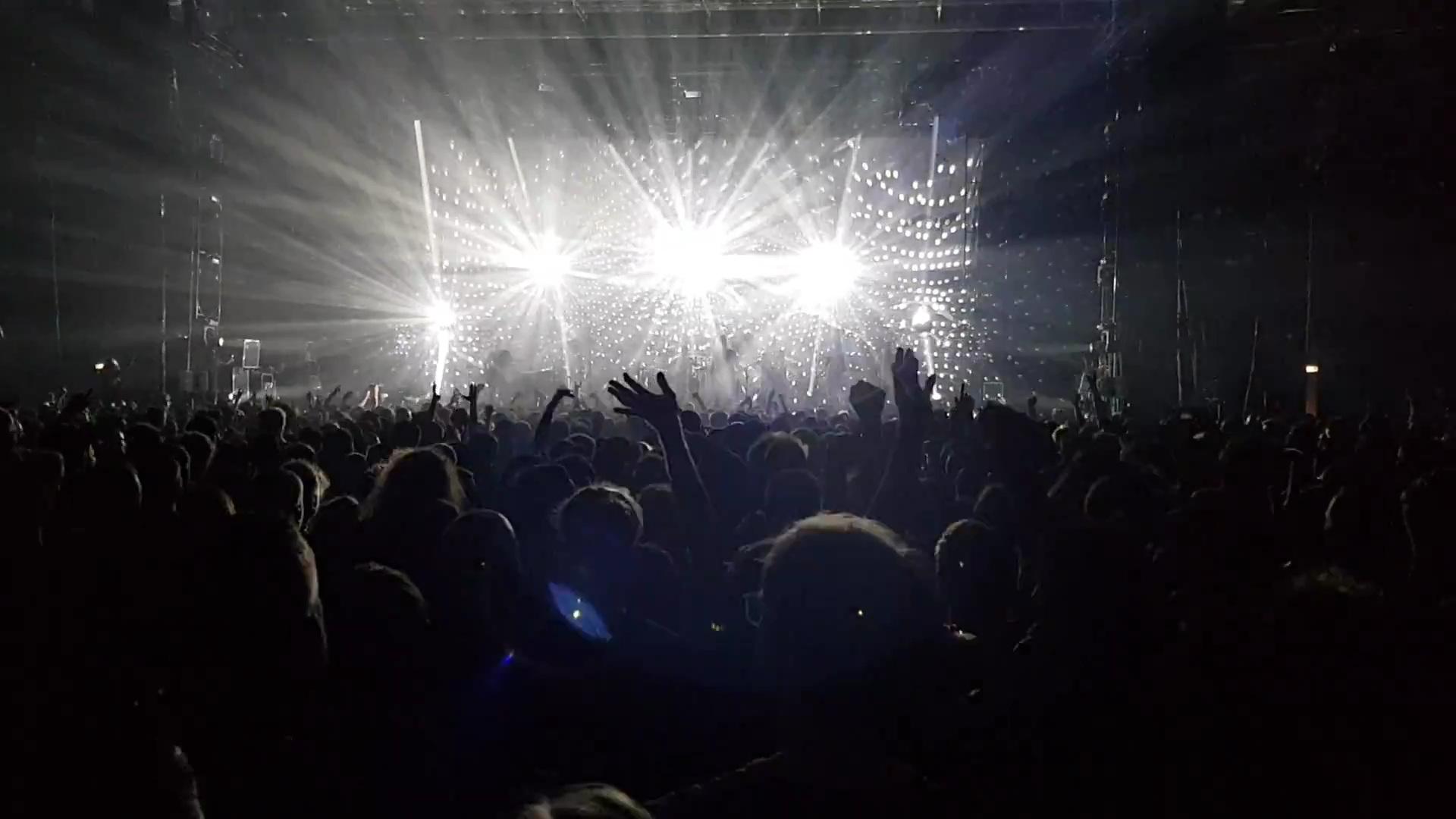 Bildbeschreibung von KI:
Das Foto zeigt eine große Menschenmenge bei einem Konzert oder einer Musikveranstaltung in einer Halle. Die Zuschauer stehen dicht gedrängt vor der Bühne, viele haben ihre Arme erhoben oder gestikulieren zur Musik. Im Hintergrund sind mehrere sehr helle Scheinwerfer zu sehen, die direkt in die Kamera leuchten. Das Licht strahlt fächerförmig nach außen und erzeugt starke Lichtstrahlen, die den Raum durchziehen. Die Bühne selbst und die Musiker sind wegen der Helligkeit und des Gegenlichts nur schemenhaft zu erkennen. An den Seiten sind Gerüste mit Technik oder Lautsprechern aufgebaut. Die Stimmung wirkt energiegeladen und ausgelassen, typisch für ein Livekonzert mit intensiver Lichtshow.
Bildbeschreibung von KI:
Das Foto zeigt eine große Menschenmenge bei einem Konzert oder einer Musikveranstaltung in einer Halle. Die Zuschauer stehen dicht gedrängt vor der Bühne, viele haben ihre Arme erhoben oder gestikulieren zur Musik. Im Hintergrund sind mehrere sehr helle Scheinwerfer zu sehen, die direkt in die Kamera leuchten. Das Licht strahlt fächerförmig nach außen und erzeugt starke Lichtstrahlen, die den Raum durchziehen. Die Bühne selbst und die Musiker sind wegen der Helligkeit und des Gegenlichts nur schemenhaft zu erkennen. An den Seiten sind Gerüste mit Technik oder Lautsprechern aufgebaut. Die Stimmung wirkt energiegeladen und ausgelassen, typisch für ein Livekonzert mit intensiver Lichtshow.