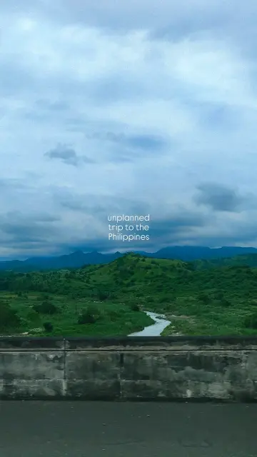 Photo of the lush Philippine countryside beneath cloudy skies, from a highway viewpoint.