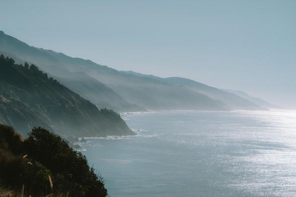 Serene coastal view with gentle waves, rolling hills, and a soft fog enveloping the landscape.