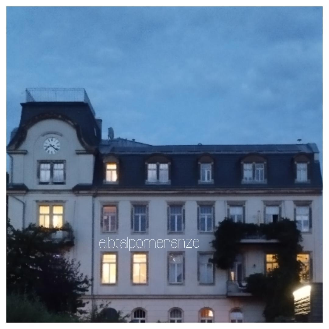 Haus aus der Gründerzeit vor blauem Abenddämmerungshimmel. Einige Fenster sind erleuchtet. Am Haus befindet sich eine Uhr mit Zifferblatt der Zeitangabe 20:20 Uhr. Zwei Balkons sind üppig bewachsen mit Grün, das bis zum Boden reicht. Haus aus der Gründerzeit vor blauem Abenddämmerungshimmel. Einige Fenster sind erleuchtet. Am Haus befindet sich eine Uhr mit Zifferblatt der Zeitangabe 20:20 Uhr. Zwei Balkons sind üppig bewachsen mit Grün, das bis zum Boden reicht.