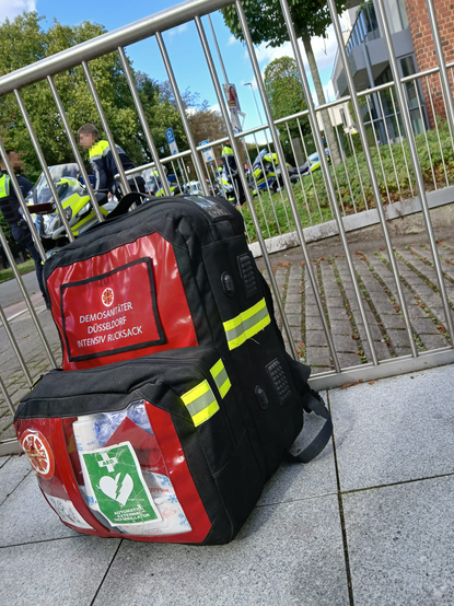 Ein Rettungsrucksack steht auf dem Boden im Hintergrund sieht man Polizei Motorräder und die dazugehörigen Polizistinnen