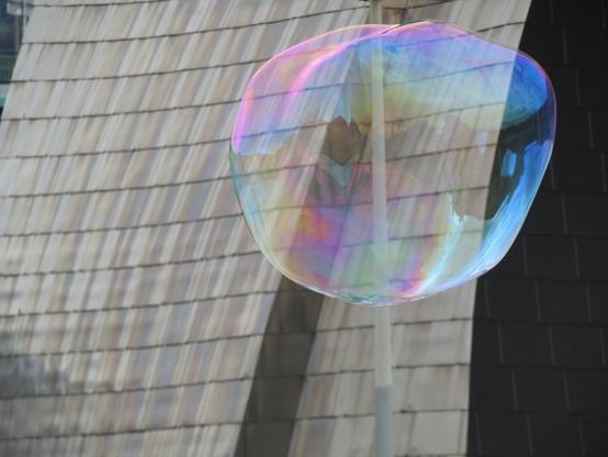 Vor der stahlgekachelten Wand des Guggenheim Museums schwebt eine grosse Seifenblase, die in allen Farben schimmert.