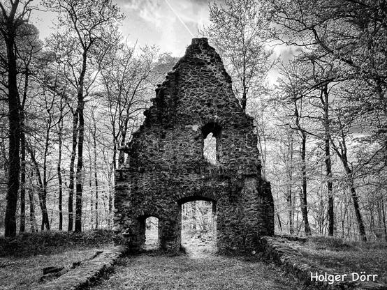 Landscape - Version: Schwarz-Weiß-Aufnahme der Kirchenruine St. Valentin bei Laubach. Die halb verfallene Mauer mit ihren Torbögen öffnet sich zum umstehenden Wald, durch den sanftes Licht fällt. Vergangenheit, Natur und Stille verschmelzen hier zu einer geheimnisvollen Atmosphäre.