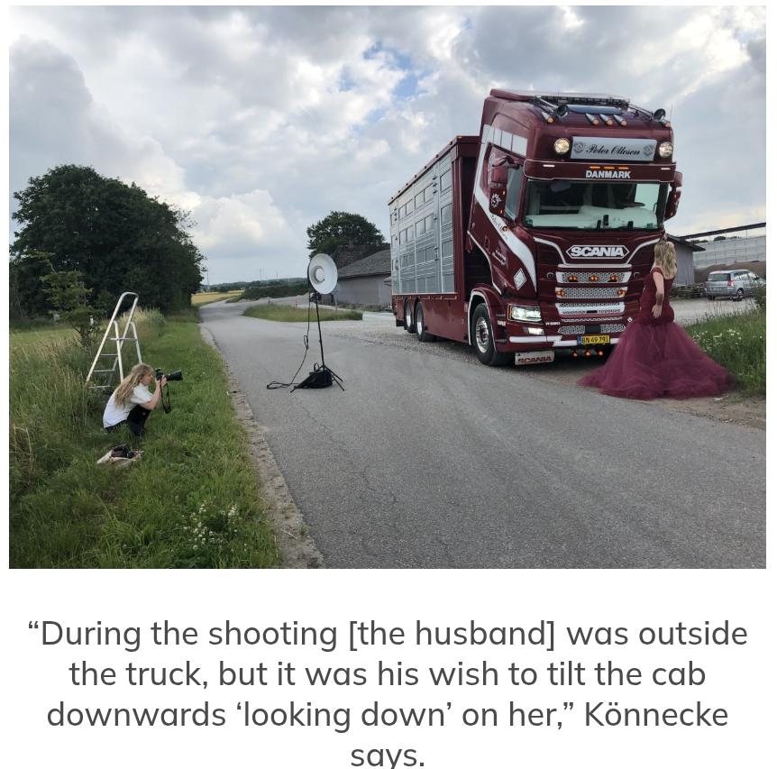 A photoshoot of a pregnant woman in a flowing dark red dress which matches the semi-trailer truck which has its cab tilted down towards her.
To the left is the photographer crouched down with a camera with a long lens.