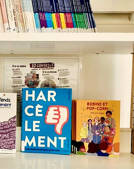 Étagère de bibliothèque montrant deux livres, le documentaire « harcèlement » et le roman « bobine et popcorn »