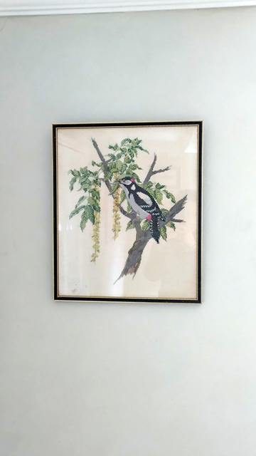 A very finely-worked piece of cross-stitch of a bird perched on a branch of a tree.