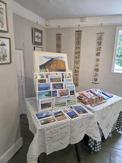 A display of handmade books and prints. They are arranged on tables that are covered in some lovely tablecloths, which are hand embroidered; part of a church fundraising effort in the 1950s.