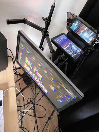 The monitor and the Elgato Prompter viewed from above so that the monitor arm that holds the monitor and the light stand can be seen.