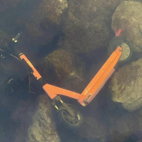 Oransj (rød) elståmoped ligger i under vann. Merket med Voi. Den blinker fortsatt.
