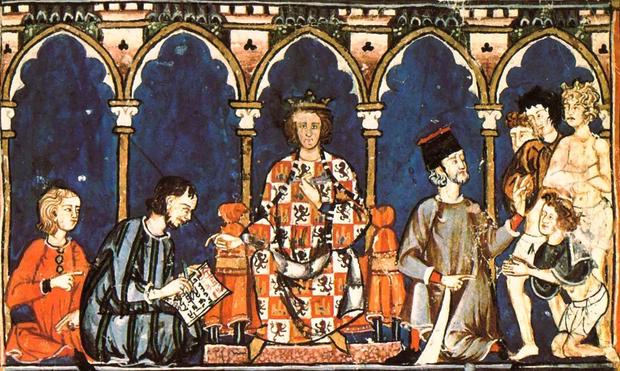 Medieval manuscript illustration from Libro de los Juegos (Alfonso X), showing a crowned figure seated on a throne in the center, flanked by advisors and attendants. The king wears a robe decorated with heraldic lions, and various figures around him appear engaged in reading, presenting, or pleading. Gothic arches frame the scene above. Though not depicting Macsen Wledig, the image evokes royal authority, mythic storytelling, and courtly power—appropriate for pairing with The Dream of Macsen.