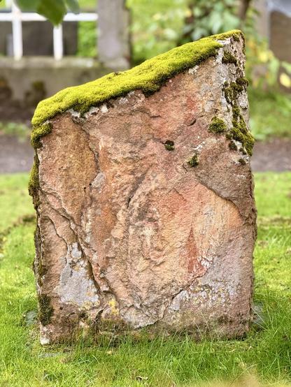 A gravestone that has an angled cut along the top side has moss growing on it