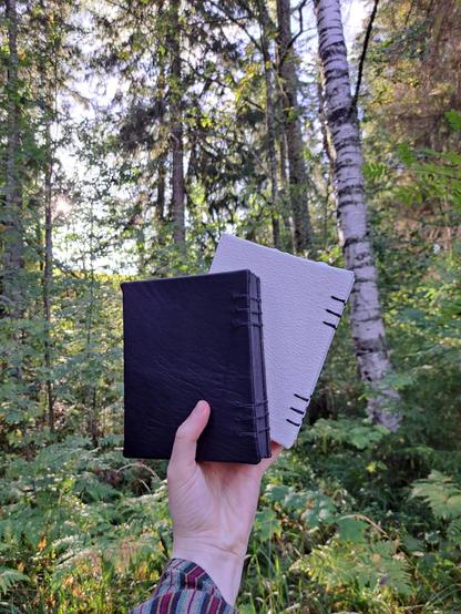 The journals shown from behind. The back covers are solid colours, the first one black and the other one bright white. The materials are second hand leather and fake leather.