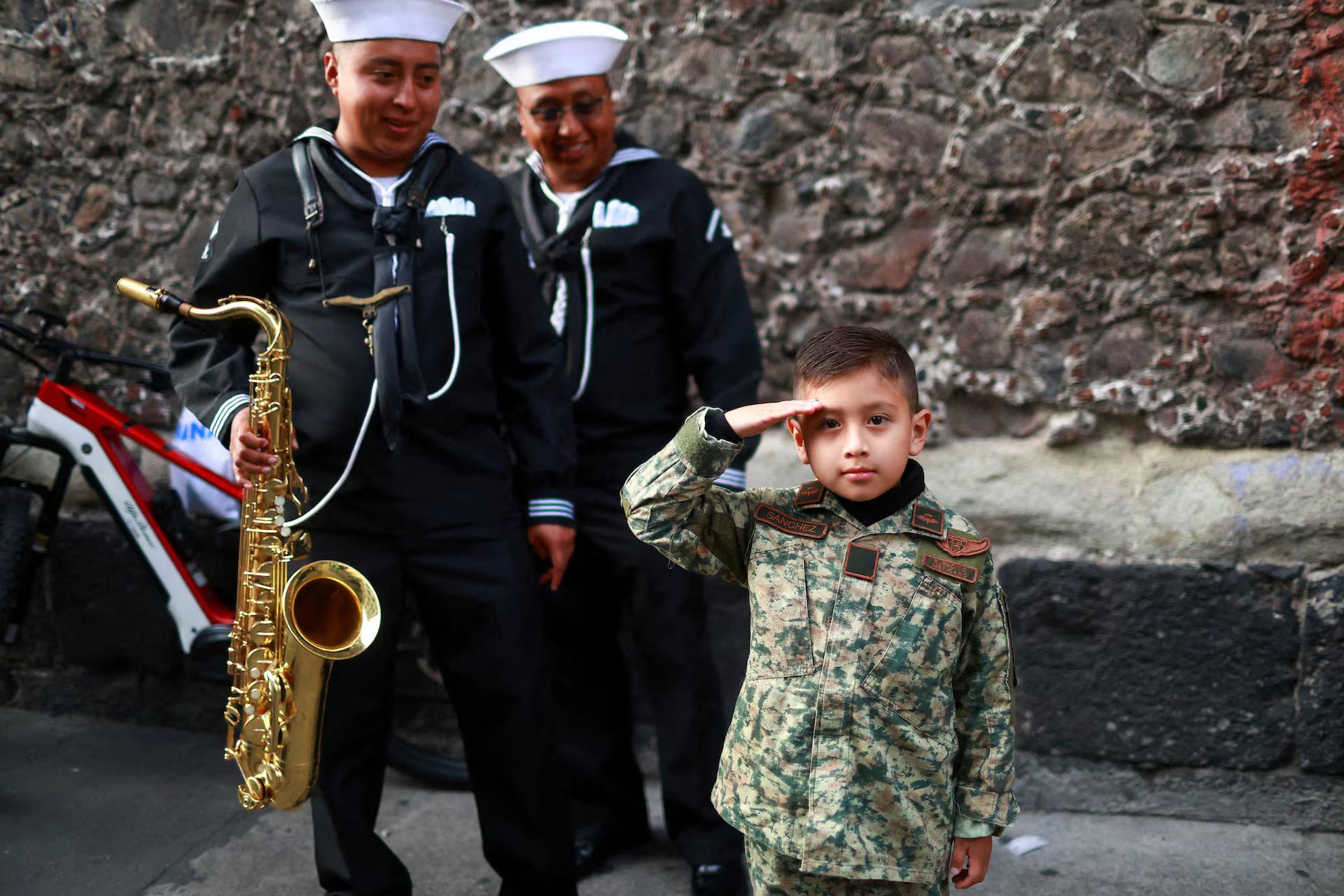 A boy salutes, next to two Navy servicemen (?), one of whom holds a saxophone.