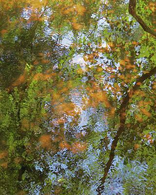 Impressionistic photograph of a pond with green and orange Autumn leaves and blue water.