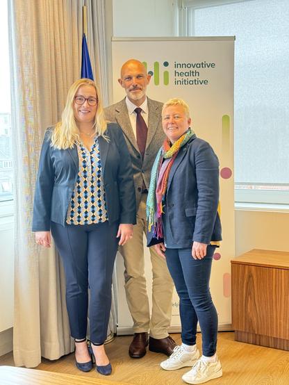 From left to right, Anna Chioti, Niklas Blomberg and Martha Cahill standing in front of an IHI banner and an EU flag.