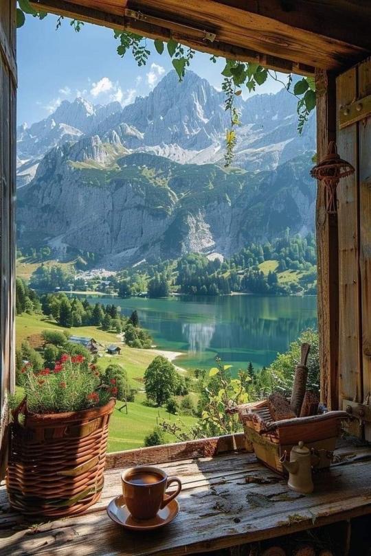 A mountain view from a window with coffee on the table.