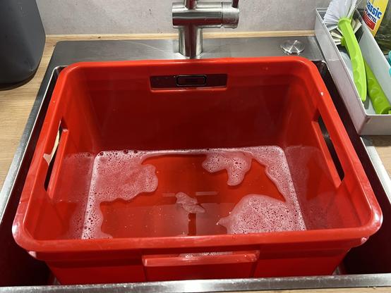 Ein großes, rechteckiges Edelstahl Spülbecken, darin steht eine große, rote Einkaufsbox aus Kunststoff mit etwas Spülwasser. 

Die Kunststoffkiste ist etwa 40 x 35 x 25 cm groß 