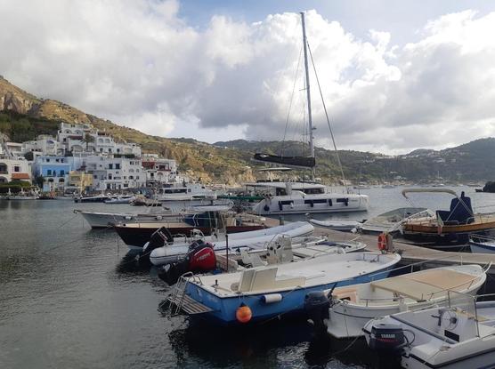 Blick auf Sant' Angelo. Links im Hintergrund bunte Häuser auf einem Hügel. In der Mitte und Rechts Hügel. Im Vordergrund Boote im Hafen.