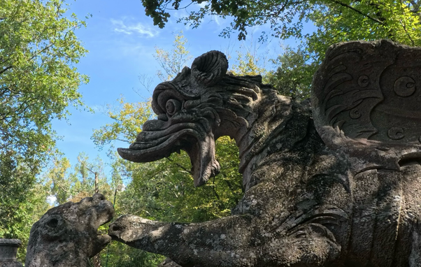 La foto mostra una panoramica della enorme statua di un drago con le fauci spalancate nel sacro bosco di Bomarzo