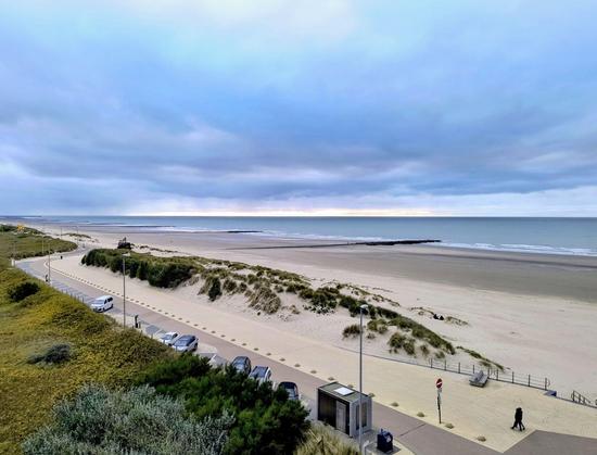 Der Blick aus dem Fenster zeigt einen breiten Sandstrand und das blaue Meer bei blauem Himmel