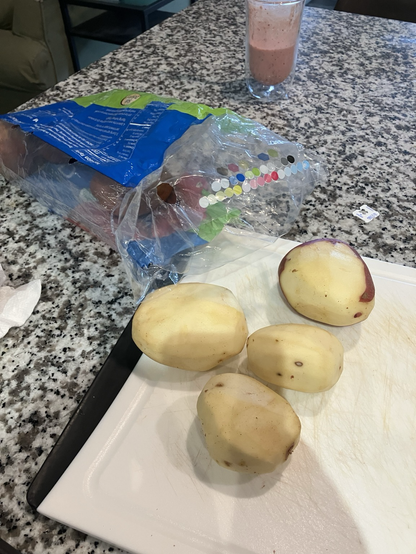 Three skinned red potatoes on top of cutting board.