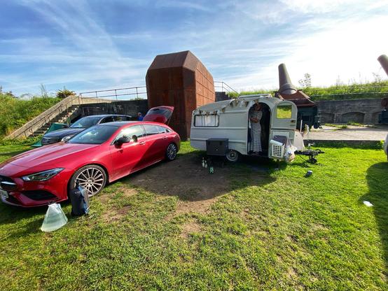 QEK Junior DDR Wohnwagen mit rotem Mercedes-Benz CLA auf einem saftig frönen Campingplatz.