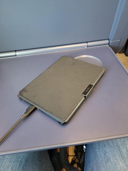 Ein Kindle liegt mit Ladekabel auf einem Klapptisch von einem ICE Sitz 