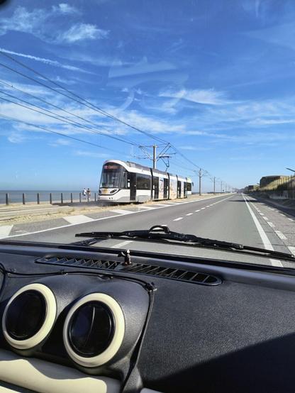 Auf dem Bild zu sehen ist der Blick aus der Frontscheibe des Aixam:
Links das Meer davor die Kustentram also die Küstenstraßenbahn, die den Aixam gerade passiert, der auf der rechten Straßenseite einer zweispurigen Straße fährt, die parallel zum Strand verläuft.