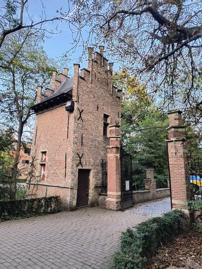 Zu sehen ist eines der Zugangsportale zum Wasserschloss, gebaut aus roten Klinkersteinen mit großen schwarzen Toren aus Schmiedeeisen